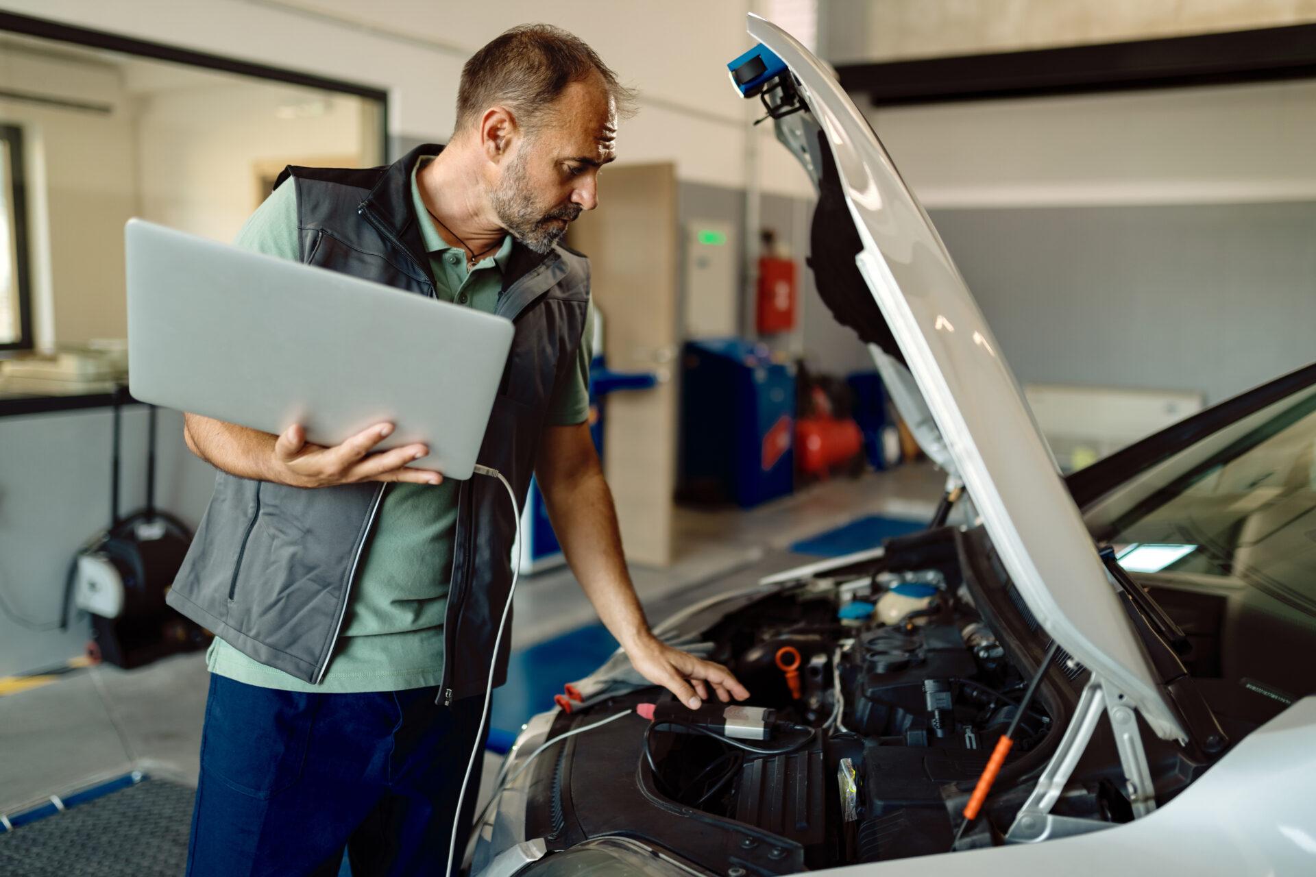 Mid adult mechanic running car diagnostic on laptop in auto repair shop.